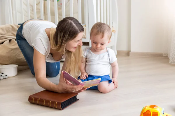 Jovem mãe deitada no chão com seu menino e livro de leitura — Fotografia de Stock