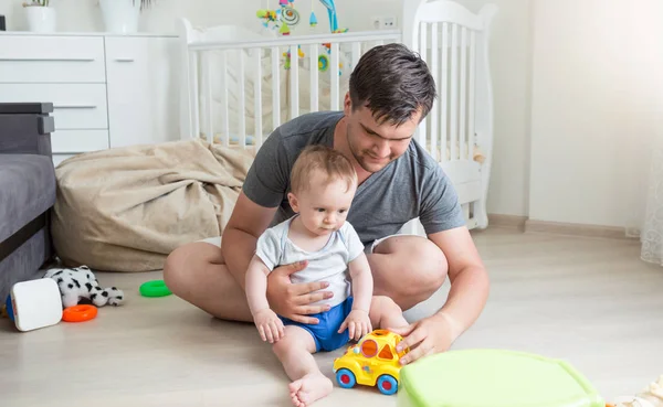 Junger Mann spielt mit seinem 10 Monate alten Jungen mit buntem Spielzeug — Stockfoto