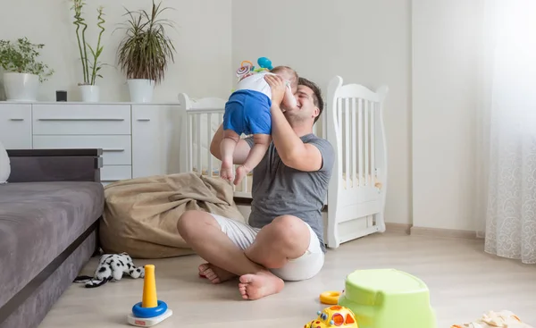 Glücklich lachender Vater sitzt mit seinem kleinen Jungen auf dem Boden und kitzelt ihn — Stockfoto