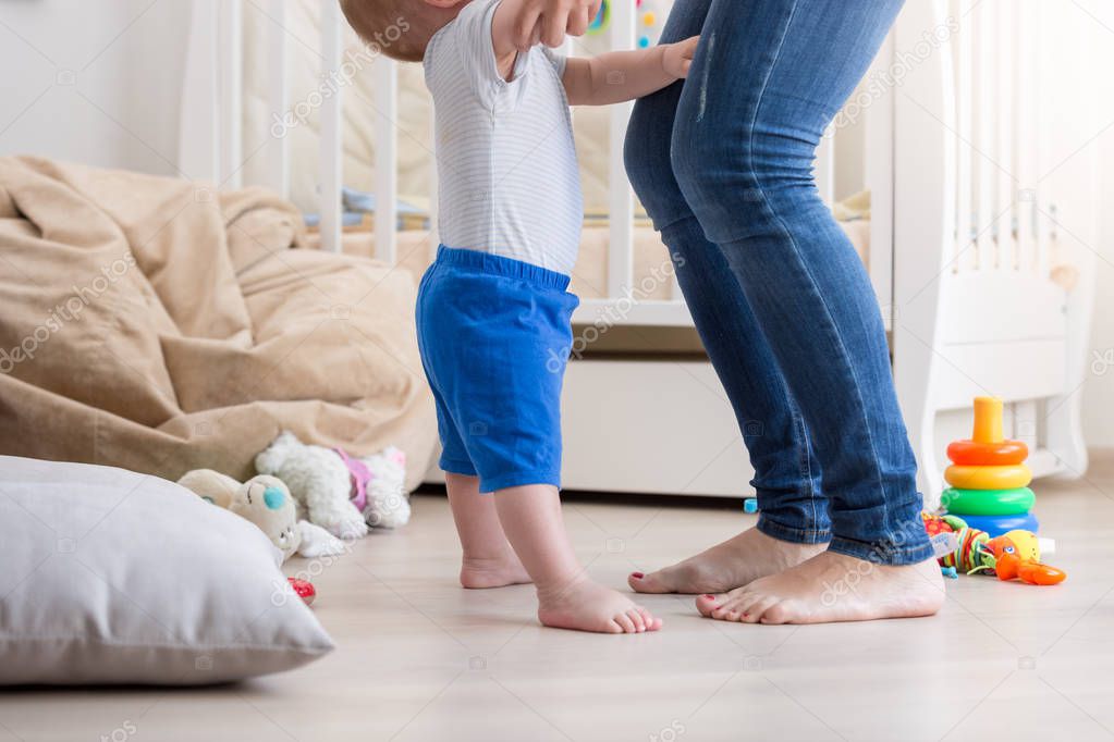 Closeup image of baby boy feet standing nest to mothers feet on floor at home