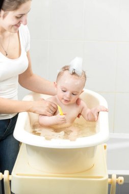 Güzel genç anne bebeğini küçük plastik banyo yıkama