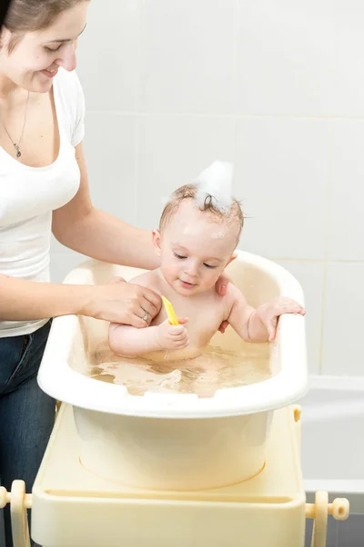 Hermosa madre joven lavando a su bebé en un pequeño baño de plástico — Foto de Stock