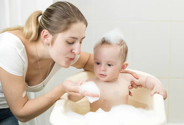 Porträt einer jungen Mutter, die mit ihrem Kleinkind spielt und sich im Badezimmer mit Schaum wäscht — Stockfoto
