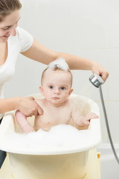 Retrato de niño lindo mirando en la cámara mientras la madre lo lava en el baño — Foto de Stock