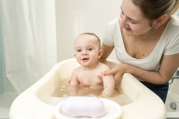 Retrato de feliz madre joven sosteniendo a su bebé sentado en un pequeño baño de plástico — Foto de Stock