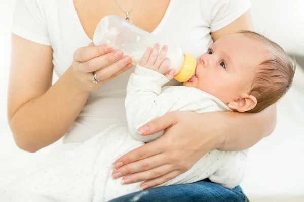 Foto de primer plano de una mujer joven sosteniendo a su bebé en el regazo y dándole una botella de leche — Foto de Stock