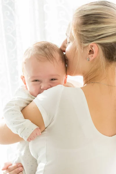 Portrait of adorable 3 months old baby boy smiling while mother kissing him in head — Stock Photo, Image