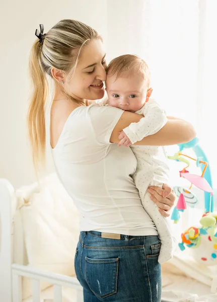 Retrato de feliz madre sonriente abrazando a su bebé en el dormitorio en la cuna —  Fotos de Stock