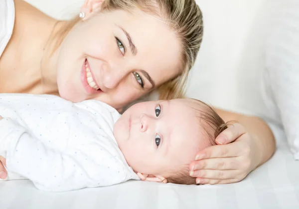 Mutlu gülümseyen anne ve bebek yatakta yatarken ve kamera seyir closeup portresi — Stok fotoğraf