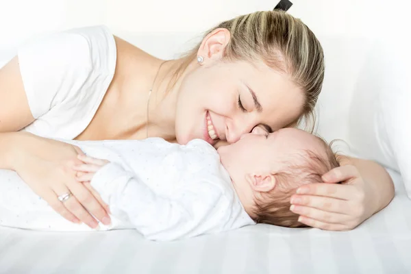 Portriat of happy young mother with closed eyes lying on bed next to her 3 months old baby boy — Stock Photo, Image