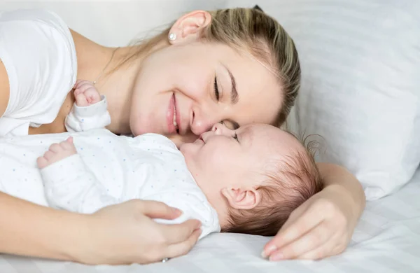 Retrato de una hermosa mujer sonriente acostada con su bebé en la cama —  Fotos de Stock