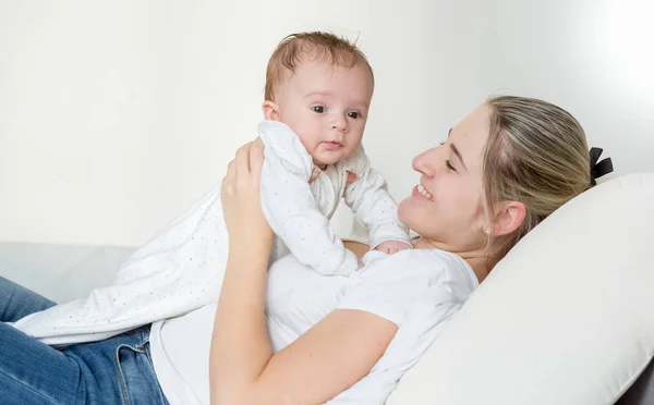 Portrait of 3 months old baby boy lying on smiling mother on bed Stock Image