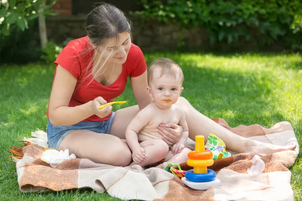 Молода мати має сімейний пікнік зі своїм маленьким хлопчиком і годує його кашею — стокове фото