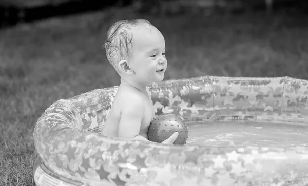 Black and white portrait of cheerful smiling baby boy playing with ball in inflatable swimming pool — Stock Photo, Image
