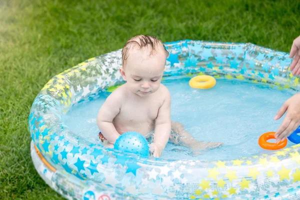 Carino bambino seduto in piscina gonfiabile e giocare con la palla blu — Foto Stock