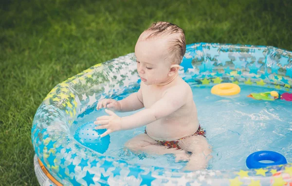 Immagine tonica di adorabile bambino che gioca nella piscina gonfiabile con palla — Foto Stock