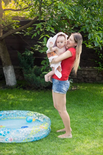 Joven madre sonriente limpiando a su hijo bebé de 10 meses después de nadar en la piscina inflable al aire libre — Foto de Stock
