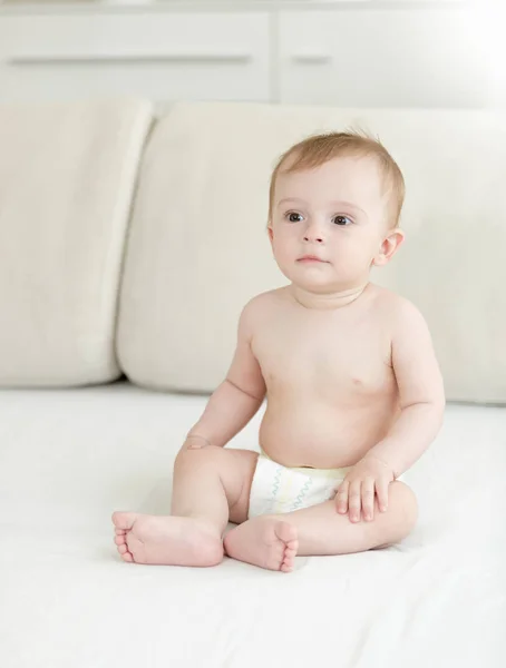 Adorable 10 months old baby boy in diapers sitting on bed