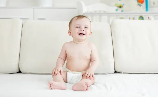 Boldog nevető totyogó fiú pelenkák ül a kanapén, és keresi a kamera — Stock Fotó