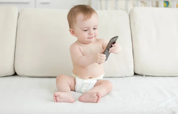 Toddler chłopiec w pieluchach, siedząc na kanapie i przy użyciu smartfona — Zdjęcie stockowe