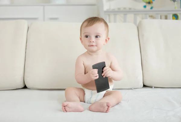 Retrato de bebé lindo niño sosteniendo el teléfono monile mientras está sentado en el sofá —  Fotos de Stock