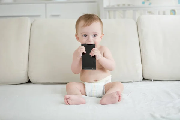 Porträtt av bedårande barn pojke sitter på soffan och bita smartphone — Stockfoto