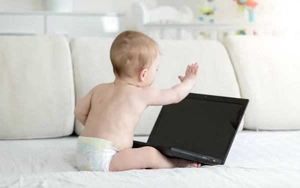Niño de 10 meses en pañales sentado en el sofá y con videoconferencia en el portátil. Puede insertar su imagen en la pantalla del ordenador portátil . —  Fotos de Stock