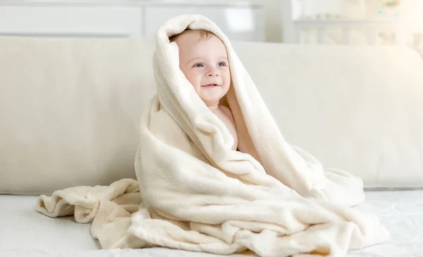 Portrait of cute 10 months old smiling baby boy sitting on bed under big blanket — Stock Photo, Image