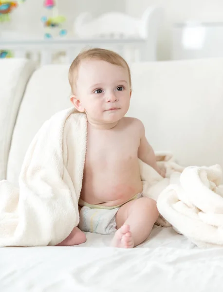 Aranyos baby boy pelenkák ül a kanapén, és amely a takaró — Stock Fotó