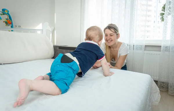 10 hónapos baba fiú ágy felé mosolygó fiatal anya csúszó — Stock Fotó