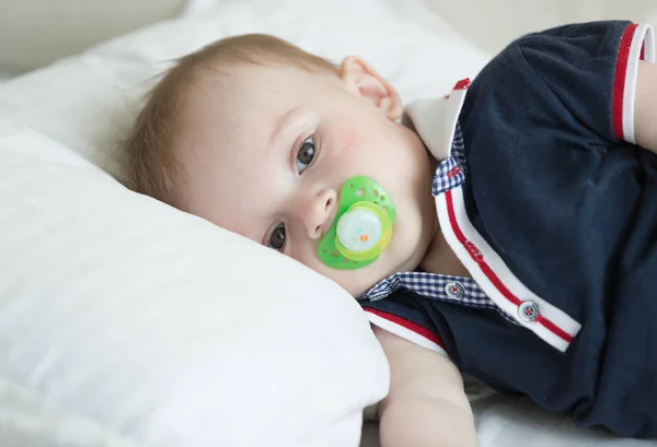 Retrato de primer plano de un bebé de 10 meses acostado sobre una almohada y sosteniendo un chupete — Foto de Stock