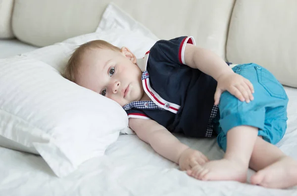 Portrait de mignon bébé garçon de 10 mois en t-shirt et short couché sur grand oreiller sur le lit — Photo