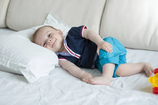 Lindo niño sonriente acostado en la cama y mirando en la cámara — Foto de Stock