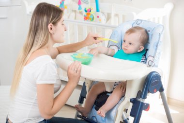 Genç anne bebek sandalyesi oturan oğlu besleme portresi