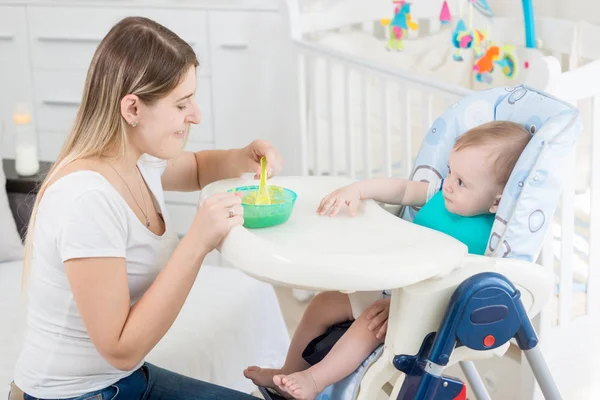 Retrato de sorrir jovem mãe alimentando seu bebê na sala de estar — Fotografia de Stock