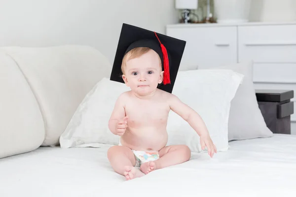 Retrato de niño divertido en gorra de graduación sentado en la cama — Foto de Stock