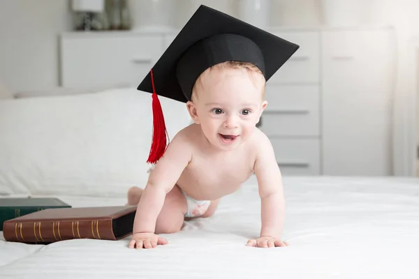 Divertida imagen de adorable bebé niño en pañales con gorra de graduación arrastrándose en la cama — Foto de Stock
