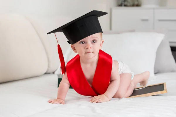 Portrait of cute baby boy in diapers and graduation hat crawling on bed — Stock Photo, Image