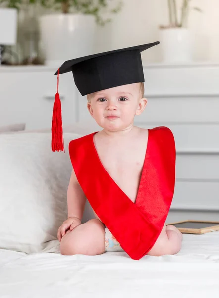 Imádnivaló baba fiú mortarboard hat és a red ribbon keresi a kamera portréja. A korai gyermek oktatás fogalmát — Stock Fotó