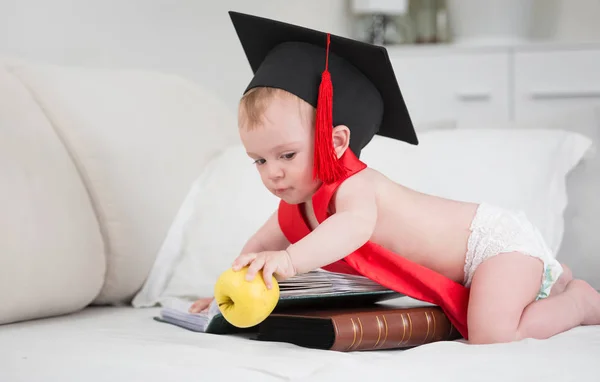 Lindo bebé con gorra de graduación alcanzando la manzana amarilla. Concepto de educación infantil temprana — Foto de Stock