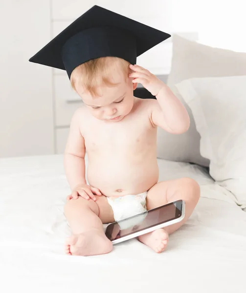Retrato tonificado de lindo bebé niño con sombrero de profesor frotando la frente mientras usa la tableta digital —  Fotos de Stock
