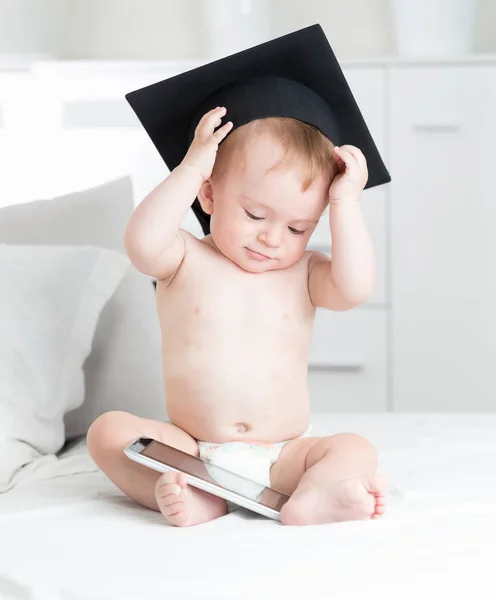 Ritratto di bambino carino in cappello di laurea guardando cartoni animati su tavoletta digitale. Concetto di bambini intelligenti e istruzione precoce con l'uso di tecnologie moderne e computer — Foto Stock