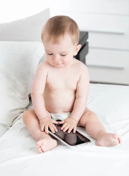 Söt baby boy i blöjor på sängen med digital tablet PC — Stockfoto