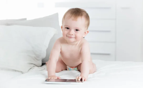 Retrato de menino sorridente em fraldas rastejando em direção ao computador tablet digital e olhando para a câmera — Fotografia de Stock