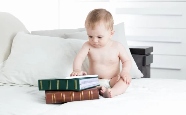 현대 기술 및 컴퓨터의 사용과 스마트 아이 조기 교육의 개념. 귀여운 아기 침대에서 책의 큰 더미와 함께 앉아 — 스톡 사진