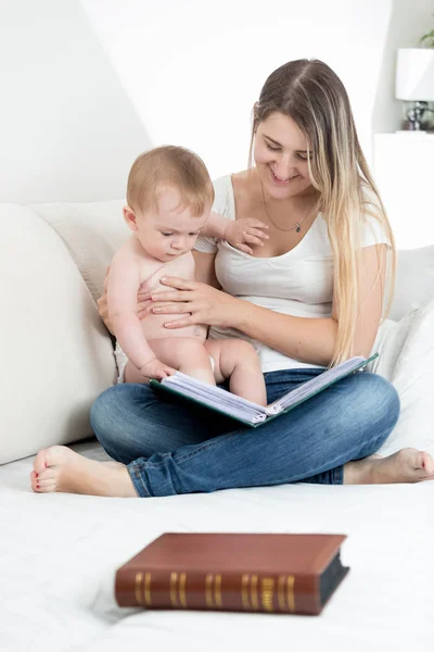 Belle jeune mère assise sur le lit avec son bébé et lisant un grand vieux livre — Photo