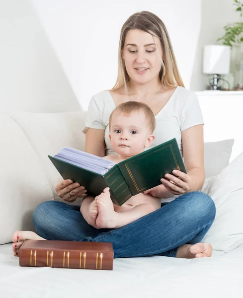 Portrét rozkošný chlapeček sedí na posteli s mladou matkou a čtení velké staré knihy — Stock fotografie