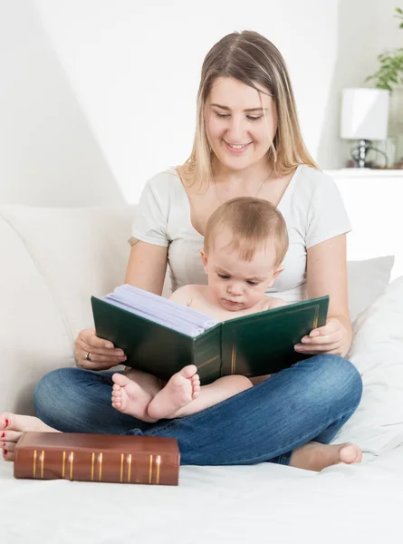 Feliz jovem mãe lendo grande livro velho para sua cama de íon bebê menino — Fotografia de Stock