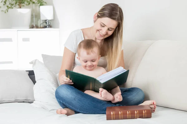 Belle jeune mère souriante lisant des histoires à son bébé garçon sur le lit — Photo