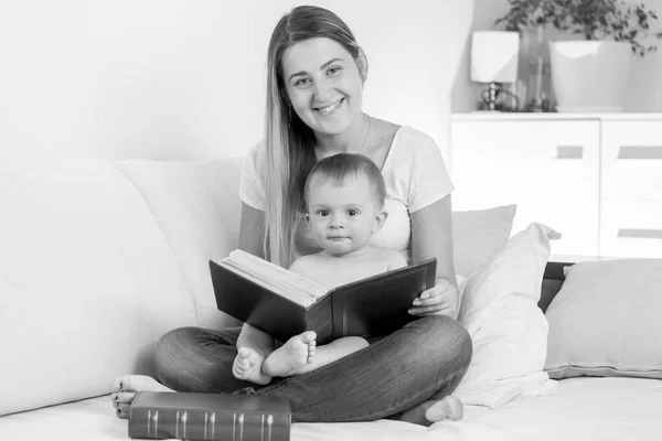 Preto e branco foto de sorrindo jovem mãe com bebê menino lendo grande velho livro — Fotografia de Stock